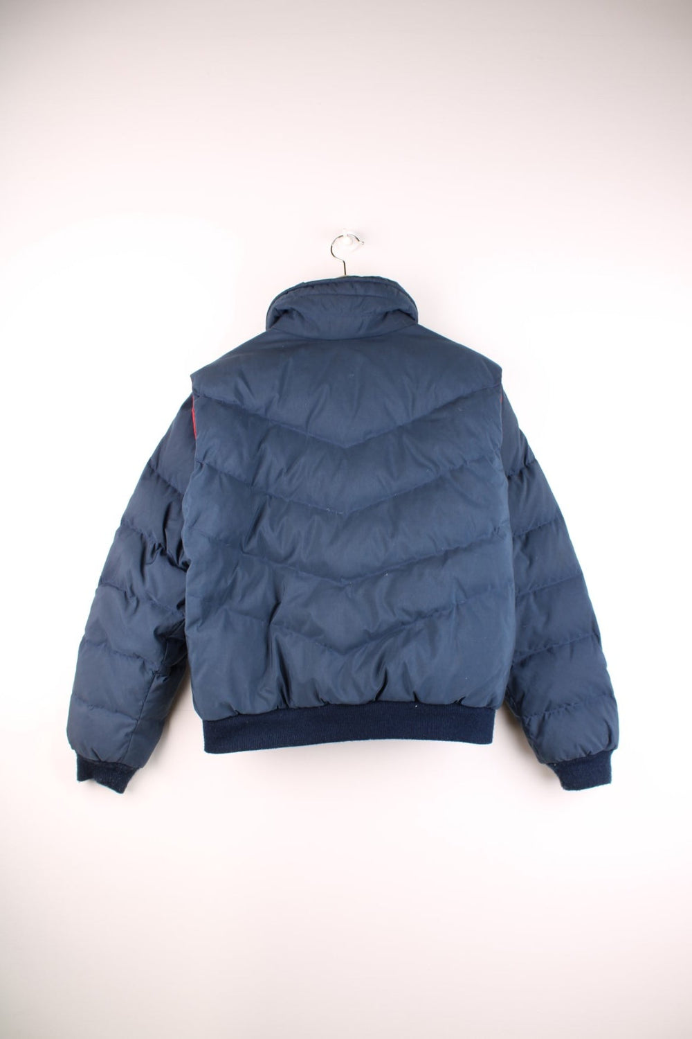 The North Face puffer coat in navy blue with red side-vents and lining, zip and snap closure, and an embroidered logo in red on the lower left sleeve.