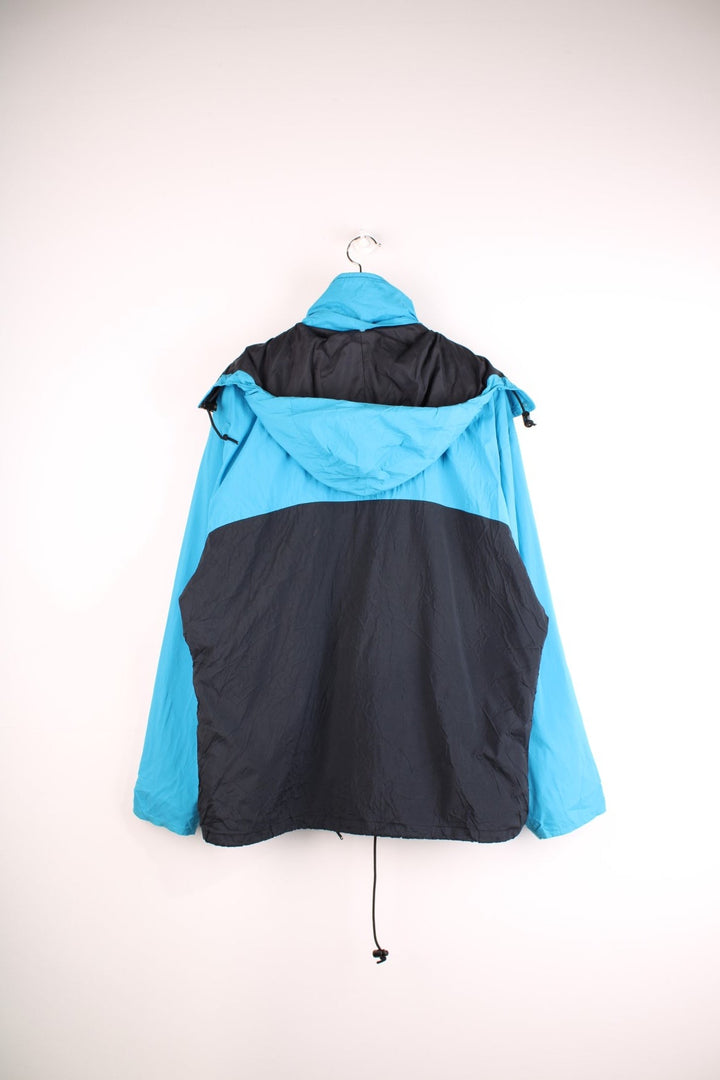 Nike ACG windbreaker jacket in black and blue with zip and snap closure, two zipped pockets, toggle adjusters, a detachable hood, and an embroidered triangle logo on the chest.