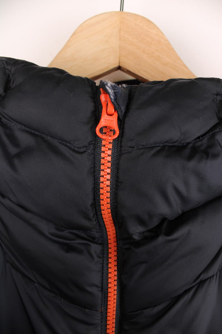 Rab puffer coat in black with orange accents and lining, zip closure, two zipped pockets, toggle adjusters, and a printed logo on the chest.