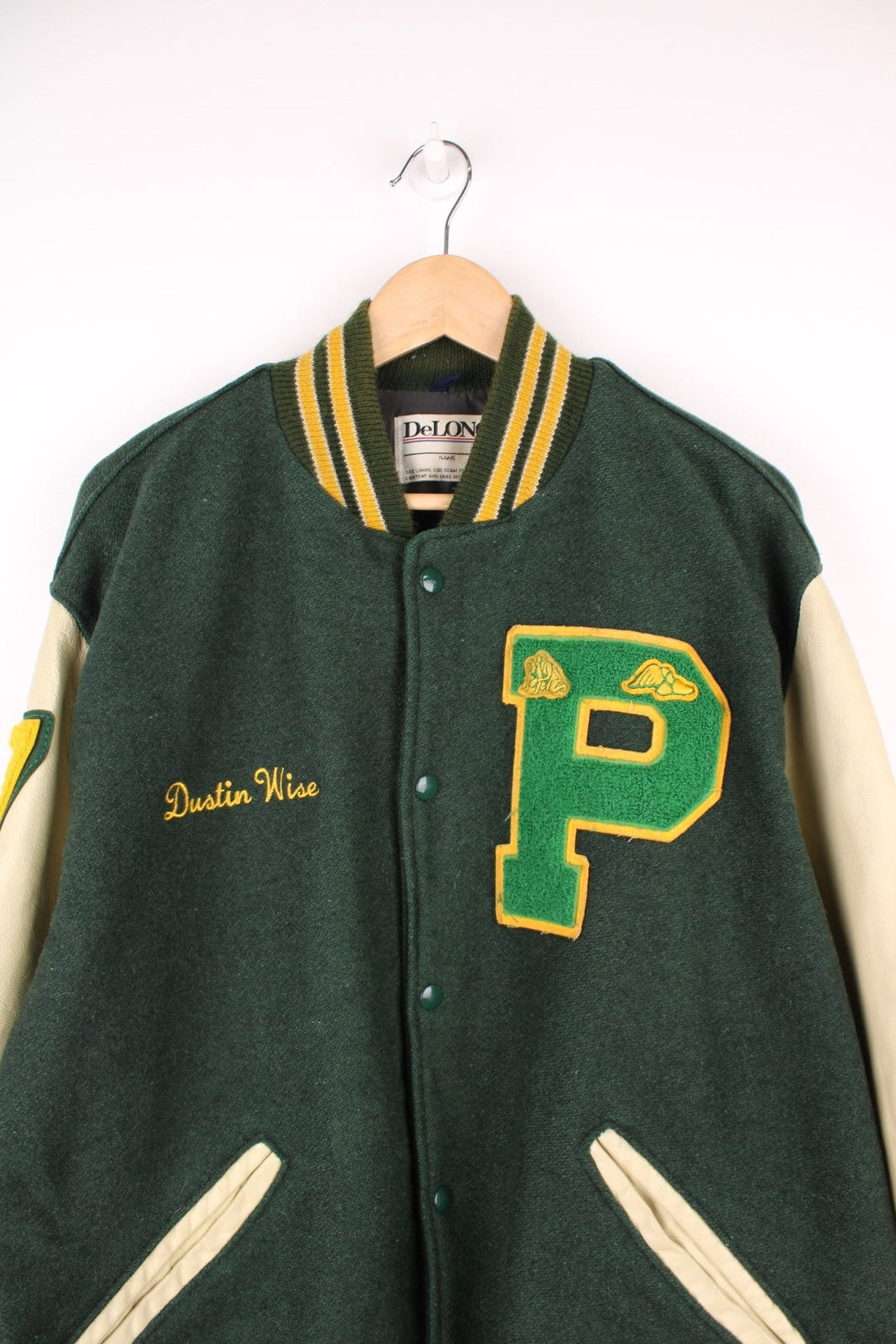 Vintage Delong, Placer Hillmen Wrestling varsity jacket in green and yellow, with beige leather sleeves and snap fastenings. Features embroidered letterman patch and numbers on the sleeve. 