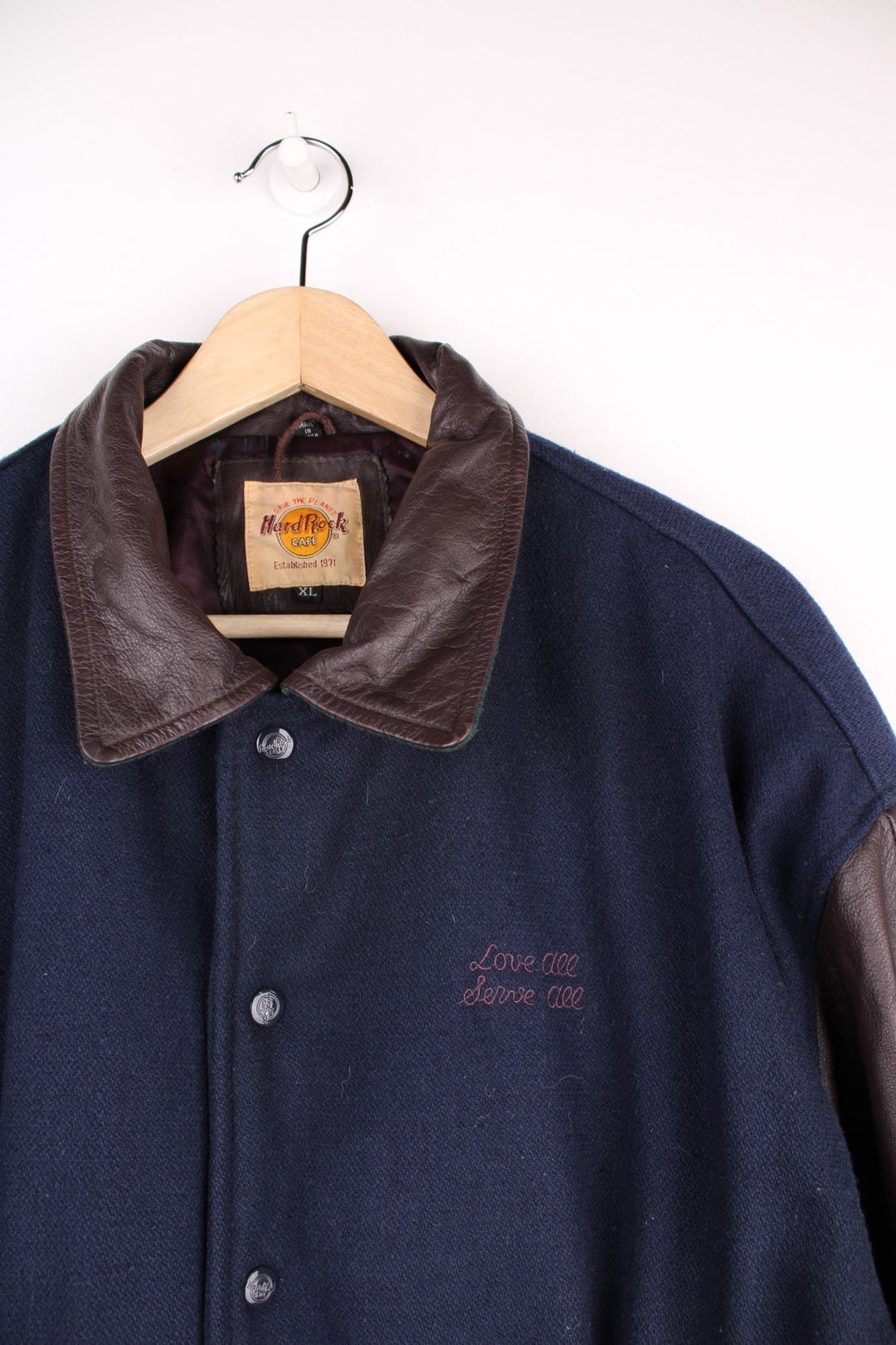 Vintage Hard Rock Cafe Jacket in a blue burgundy and green colourway. The jacket has leather sleeves, a green elasticated cuff and hem and Hard Rock logo press studs to close. On the back panel there is the - Hard Rock Cafe London - patch embroidery. The jacket also has one interior pocket and is lined with a quilted polyester filling.  