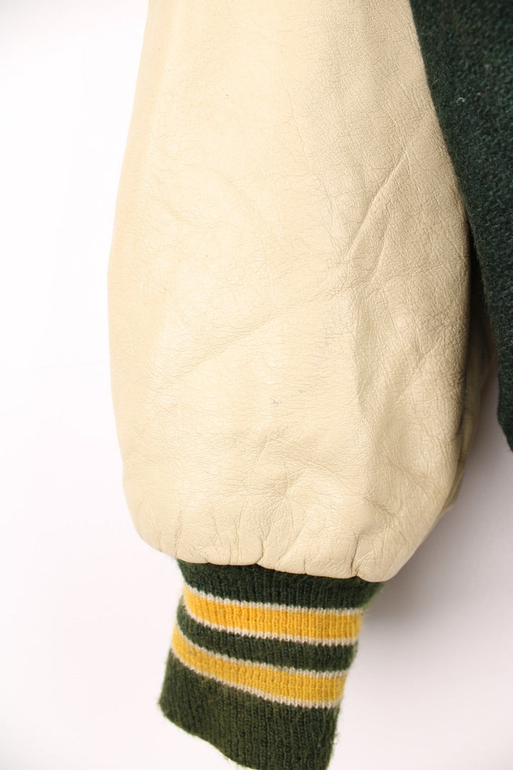 Vintage Delong, Placer Hillmen Wrestling varsity jacket in green and yellow, with beige leather sleeves and snap fastenings. Features embroidered letterman patch and numbers on the sleeve. 