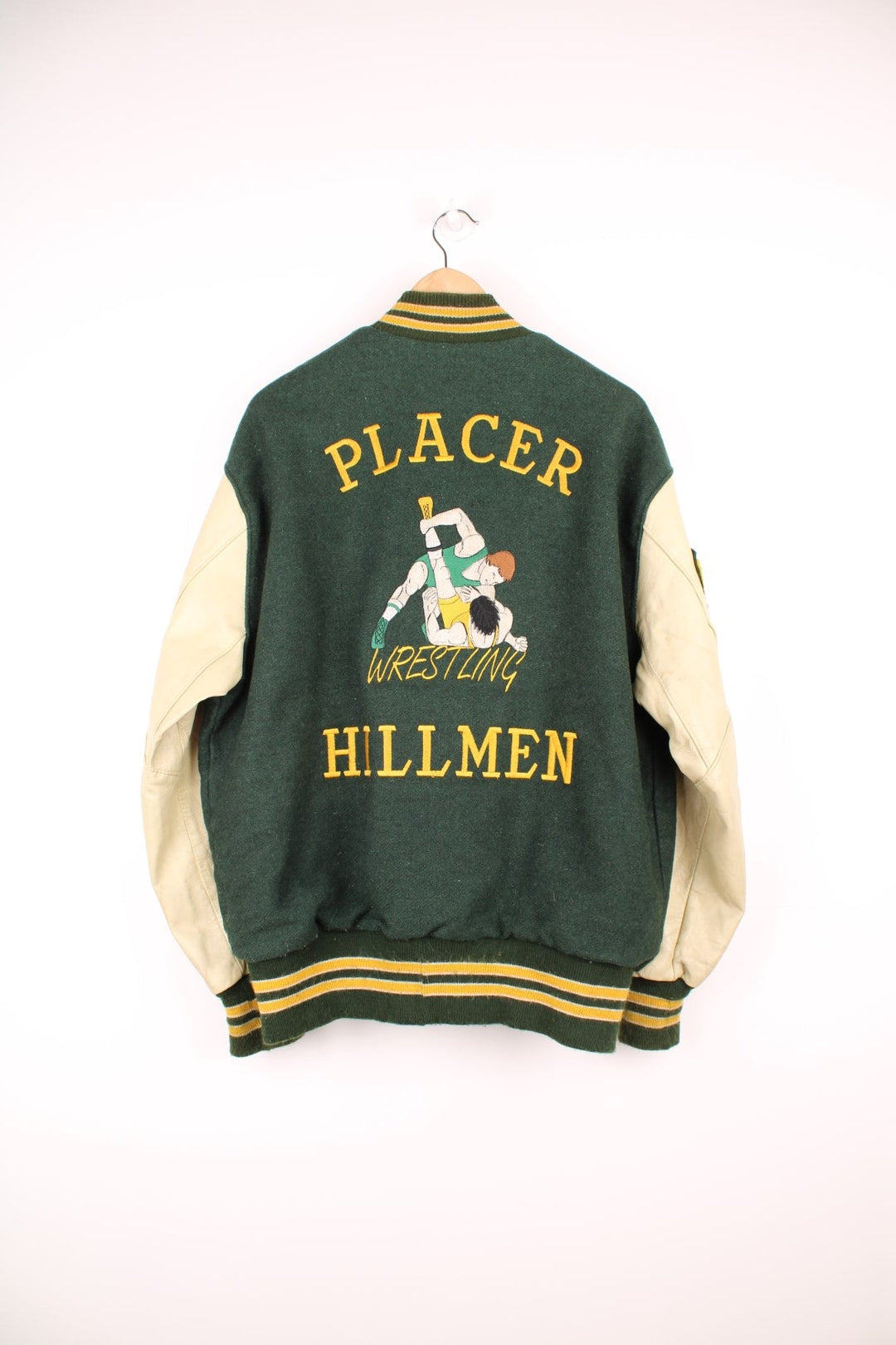 Vintage Delong, Placer Hillmen Wrestling varsity jacket in green and yellow, with beige leather sleeves and snap fastenings. Features embroidered letterman patch and numbers on the sleeve. 