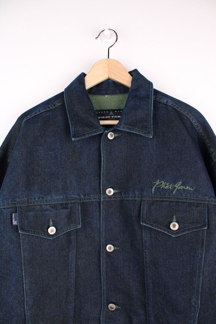 Vintage denim jacket in a dark indigo blue colourway. The jacket has two front packets, and an embroidered logo on the chest panel. On the yoke is a small Phat Farm embroidered patch. The back hem has a leather denim label stitched on.  