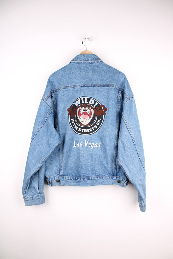 Vintage 1996 Warner Bros Vintage jacket in a mid blue denim colourway. The jacket closes with looney tunes silver buttons, has four front pockets and a large Taz embroidered patch on the back. The patch has some slight discolouration as seen from the photos. 