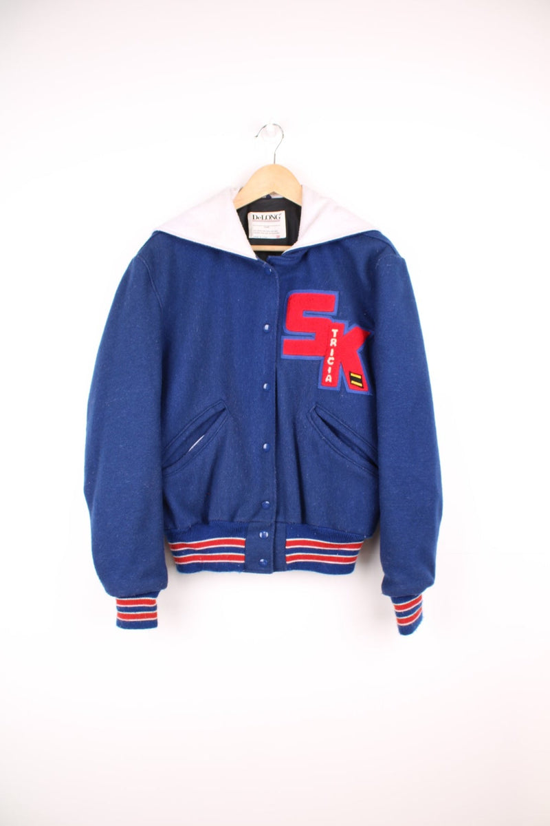 Vintage Delong varsity jacket in blue with red letterman patches, snap fastenings, and flap hood with embroidered "Drill Team".