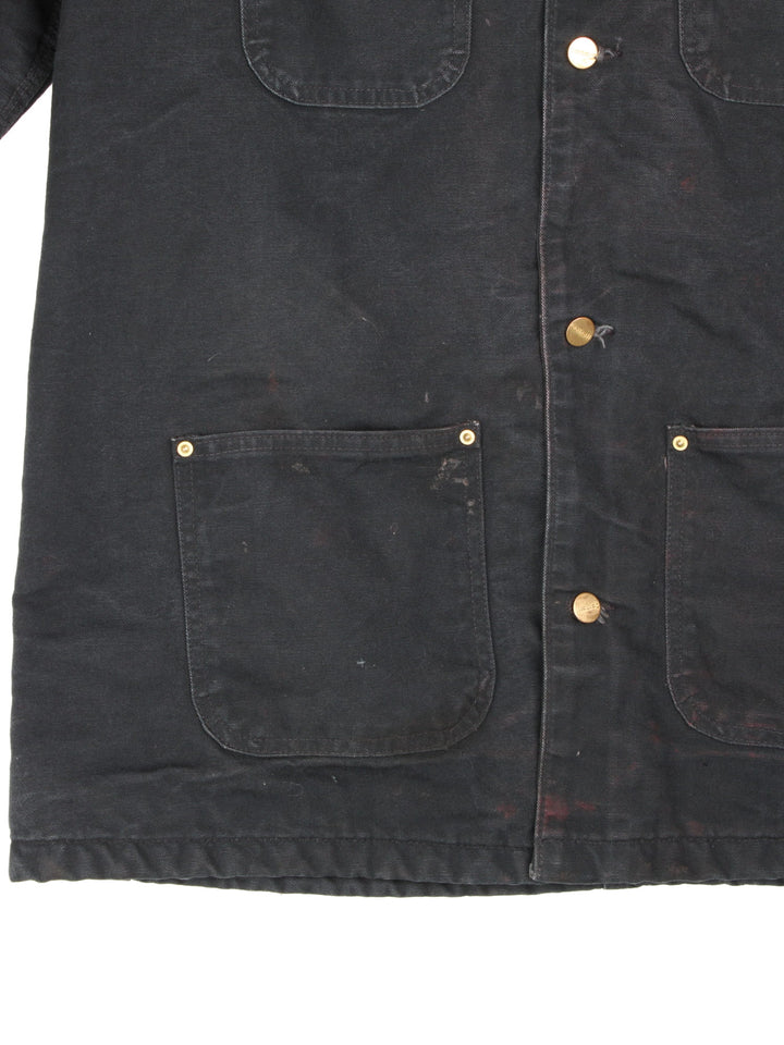  1990s Carhartt Chore jacket in a black colourway. The jacket has a corduroy collar, is blanket lined and has multiple pockets on the exterior and one on the interior. There is a stitched logo on the front pocket, and gold hardware. 