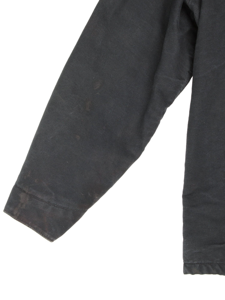  1990s Carhartt Chore jacket in a black colourway. The jacket has a corduroy collar, is blanket lined and has multiple pockets on the exterior and one on the interior. There is a stitched logo on the front pocket, and gold hardware. 