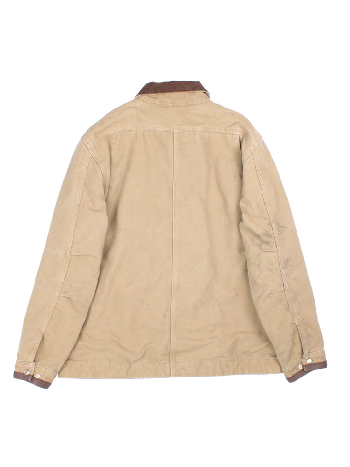 Carhartt J285 FRB Frontier Chore jacket in a tan colourway. The jacket has multiple pockets on the exterior with zip closures, and two interior pockets. There is a contrasting collar, and silver hardware. 