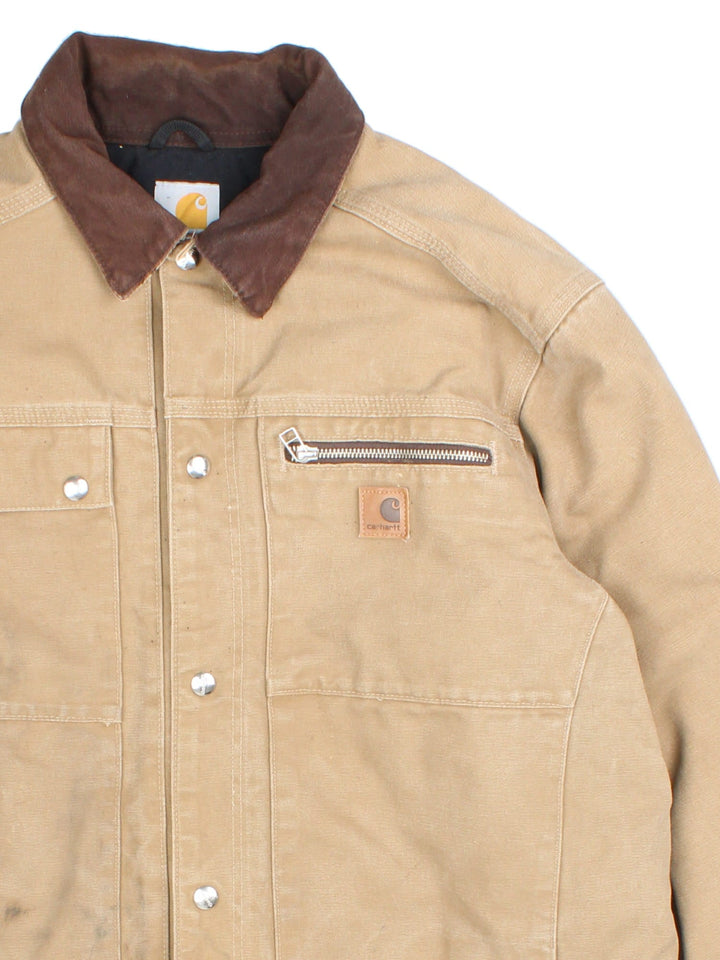 Carhartt J285 FRB Frontier Chore jacket in a tan colourway. The jacket has multiple pockets on the exterior with zip closures, and two interior pockets. There is a contrasting collar, and silver hardware. 