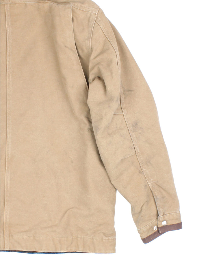 Carhartt J285 FRB Frontier Chore jacket in a tan colourway. The jacket has multiple pockets on the exterior with zip closures, and two interior pockets. There is a contrasting collar, and silver hardware. 