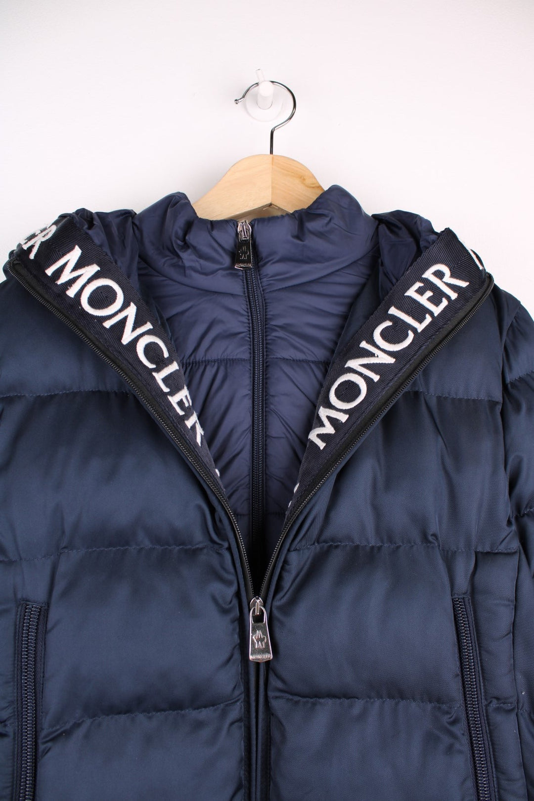 Moncler Cardere down puffer coat in a navy blue colourway. The coat has a puffer lining and the Moncler logo embroidered around the collar. There are extra thermal lined cuffs and a double zip for extra warmth.  