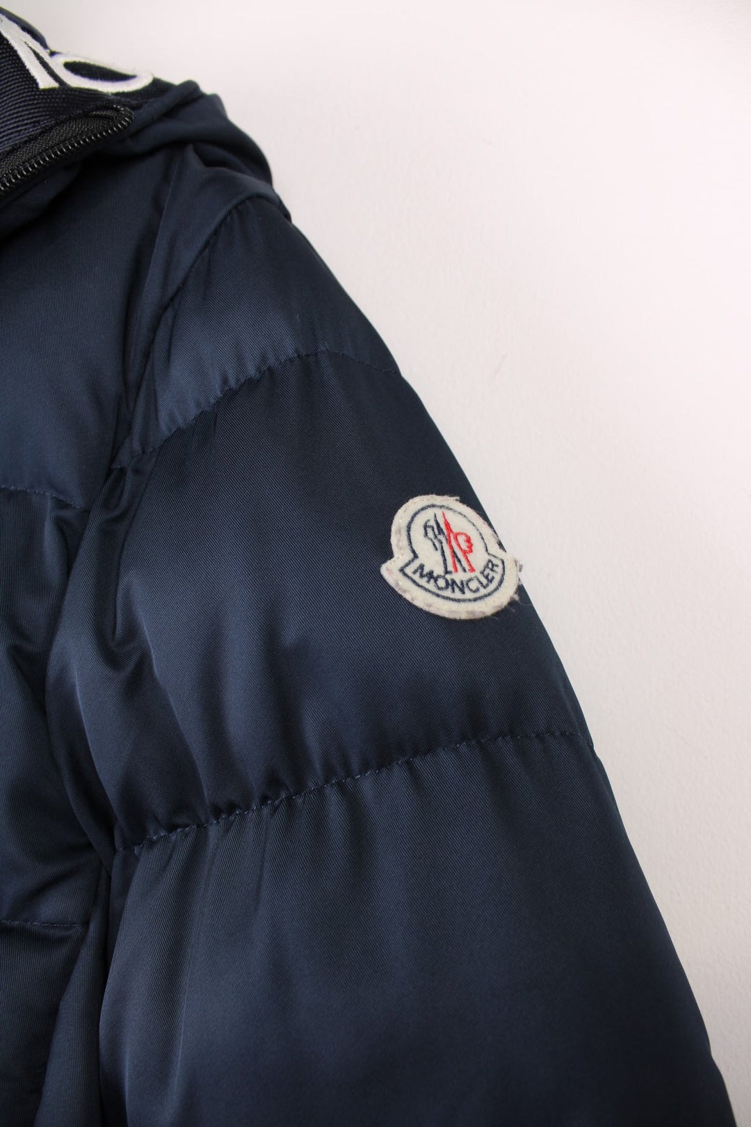 Moncler Cardere down puffer coat in a navy blue colourway. The coat has a puffer lining and the Moncler logo embroidered around the collar. There are extra thermal lined cuffs and a double zip for extra warmth.  