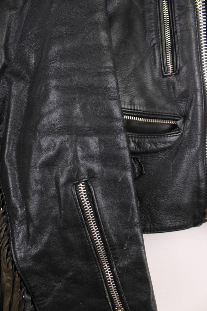 Vintage fringed motorcycle jacket in black. The jacket dates to the 1980s from the brand Drag Specialties. It is made from a heavyweight leather and has fringe up the seam of the sleeves and across the yoke panel. 