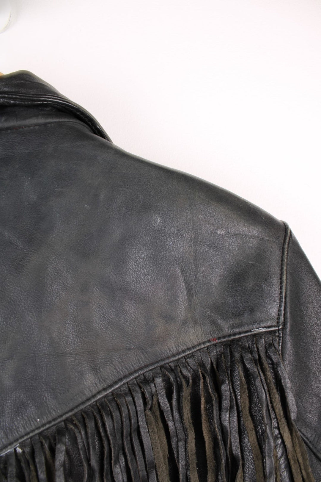 Vintage fringed motorcycle jacket in black. The jacket dates to the 1980s from the brand Drag Specialties. It is made from a heavyweight leather and has fringe up the seam of the sleeves and across the yoke panel. 