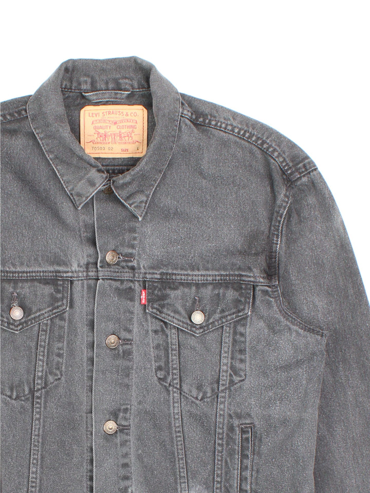 Levi Strauss denim trucker jacket in black with four pockets, button closure, and a red tab on the front.