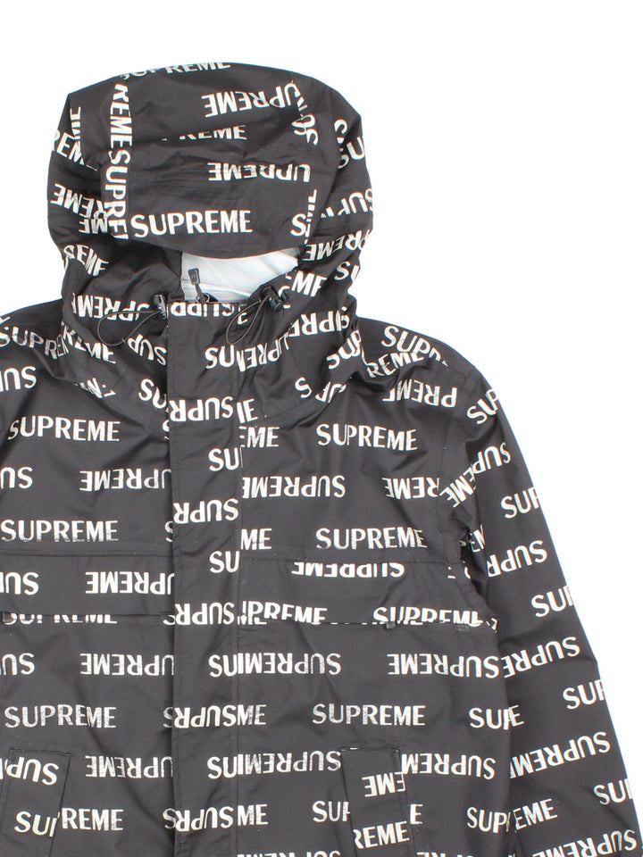 Supreme 3M reflective repeat logo taped seam waterproof jacket in black with zip and snap closure, and a hood with elastic toggle adjusters.