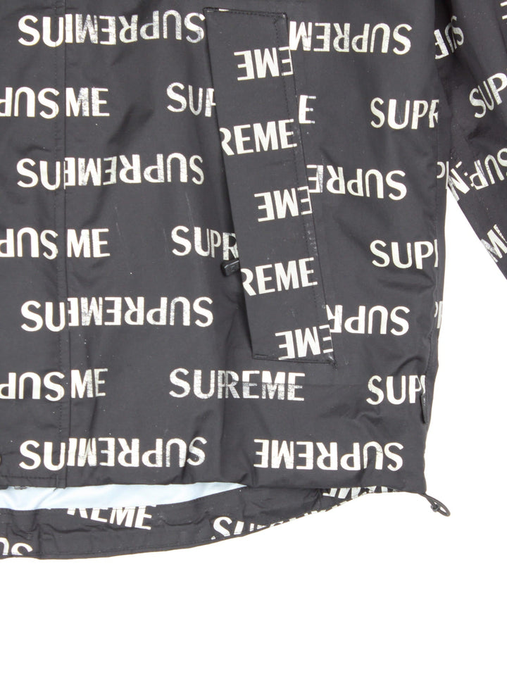 Supreme 3M reflective repeat logo taped seam waterproof jacket in black with zip and snap closure, and a hood with elastic toggle adjusters.