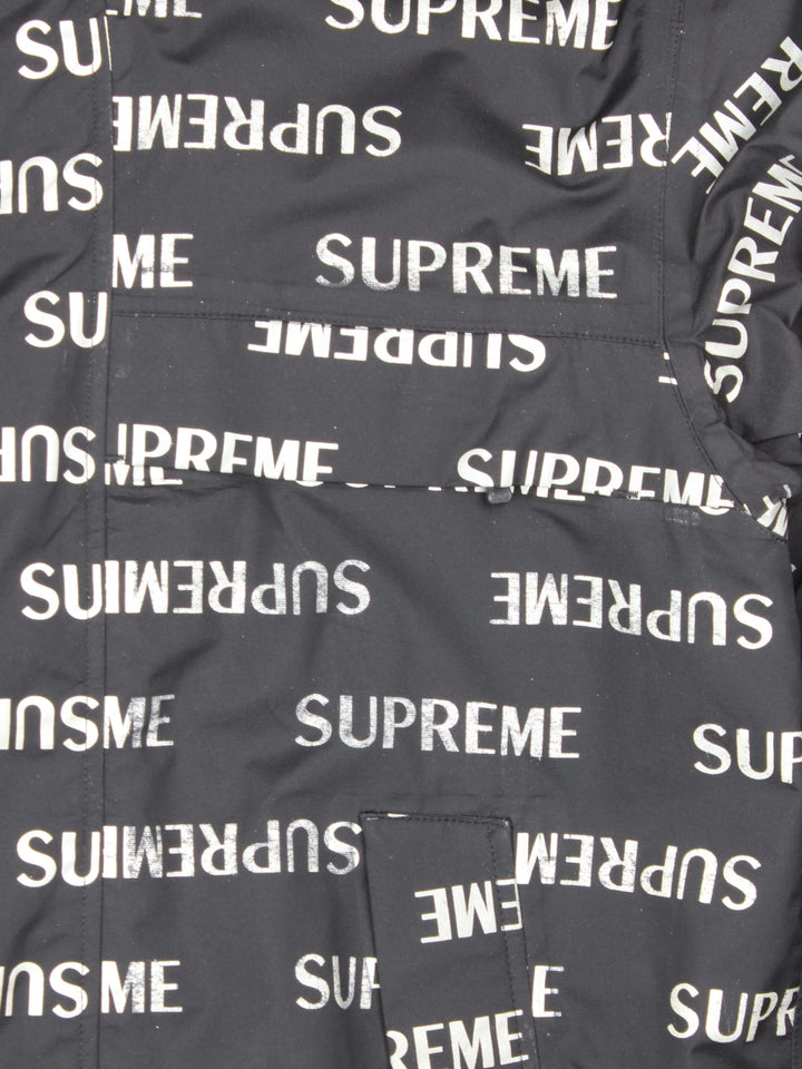 Supreme 3M reflective repeat logo taped seam waterproof jacket in black with zip and snap closure, and a hood with elastic toggle adjusters.