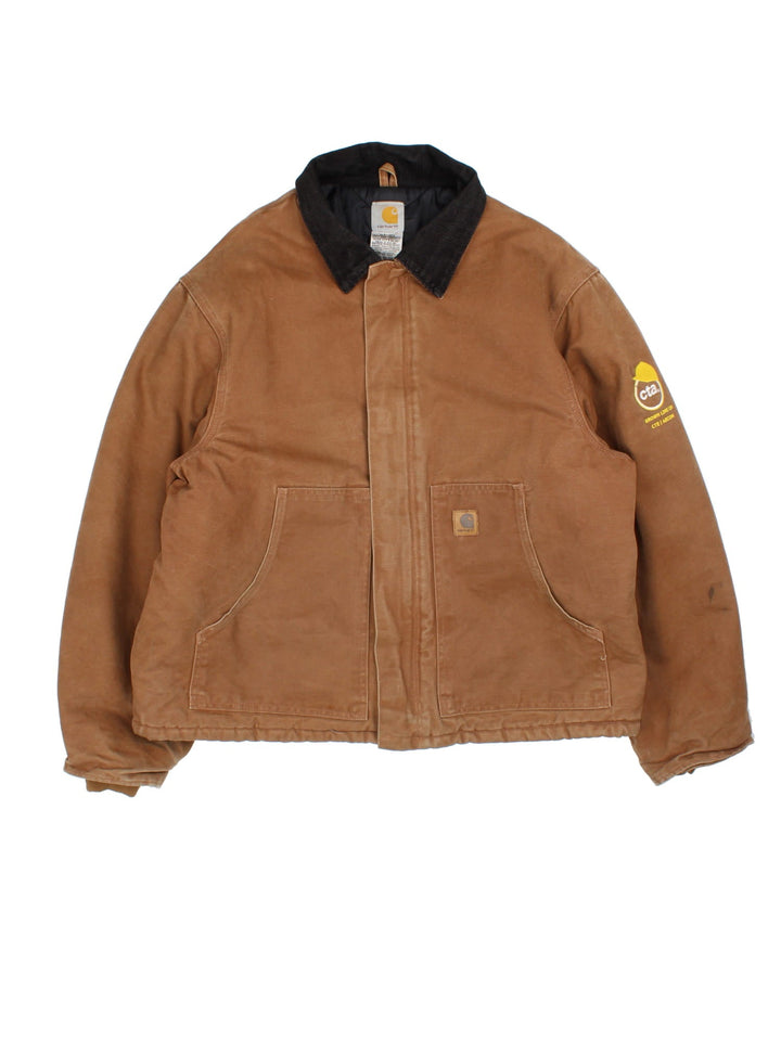 Carhartt Arctic Jacket in a brown colourway with full zip and double pocket on the front. Suede collar, Carhartt classic logo on the front pocket and a logo on the sleeve.