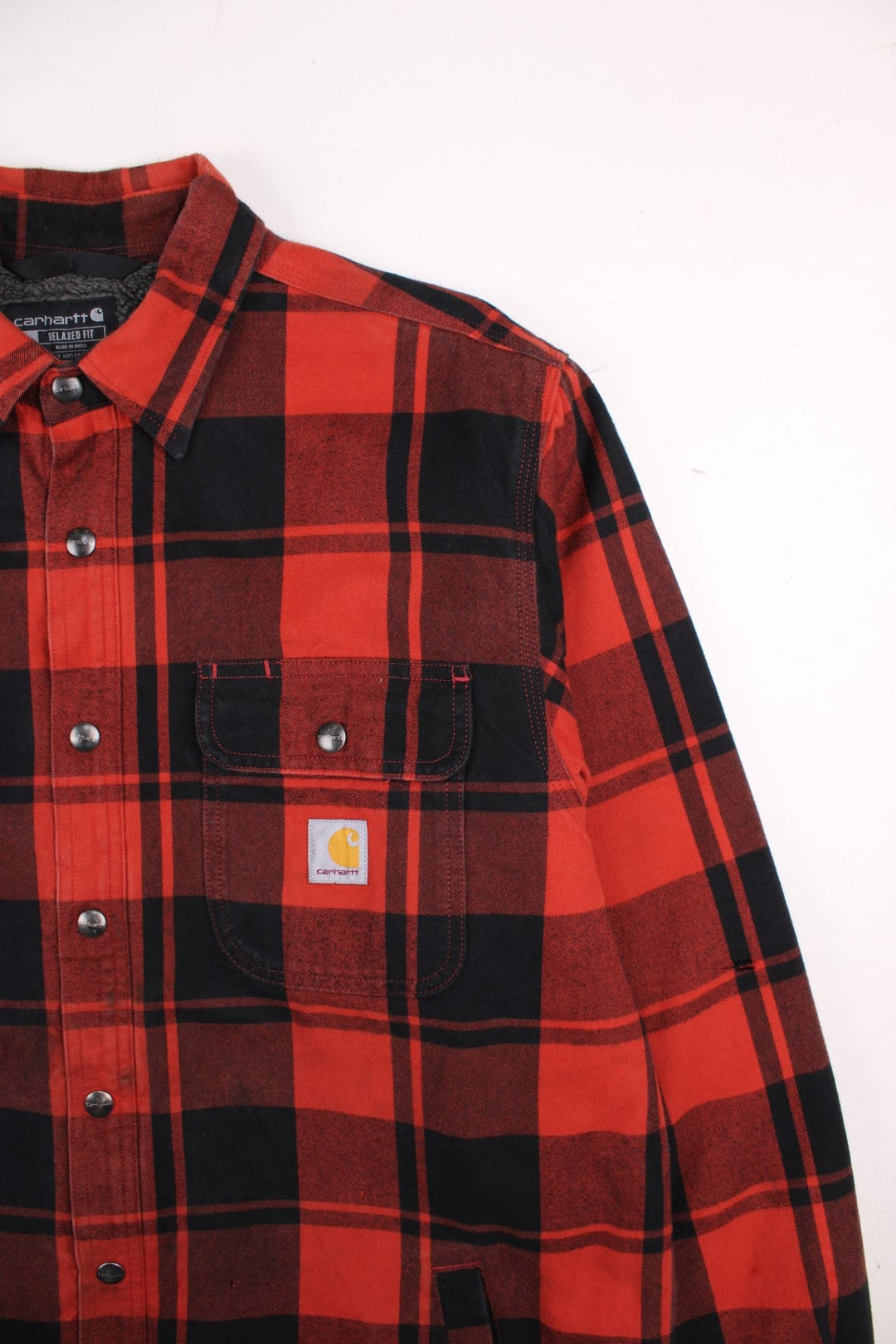 Carhartt Flannel Shirt Jacket in a red and black plaid colourway. Buttons up and has double chest pockets, insulated with a sherpa lining, and has the logo embroidered on the front.