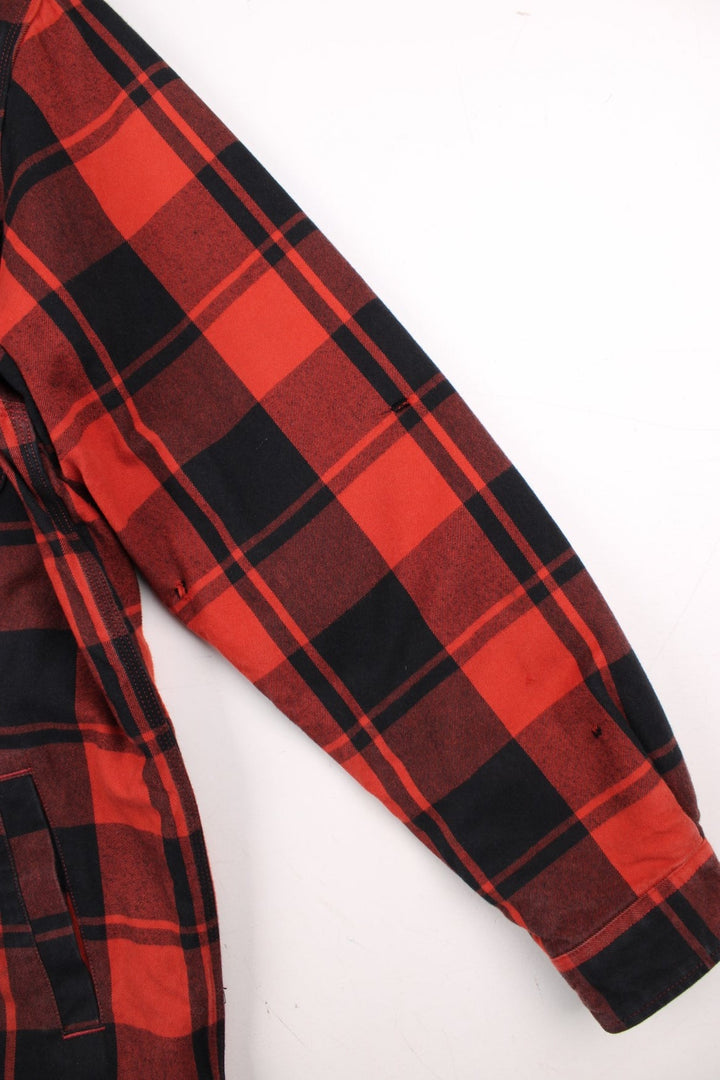 Carhartt Flannel Shirt Jacket in a red and black plaid colourway. Buttons up and has double chest pockets, insulated with a sherpa lining, and has the logo embroidered on the front.