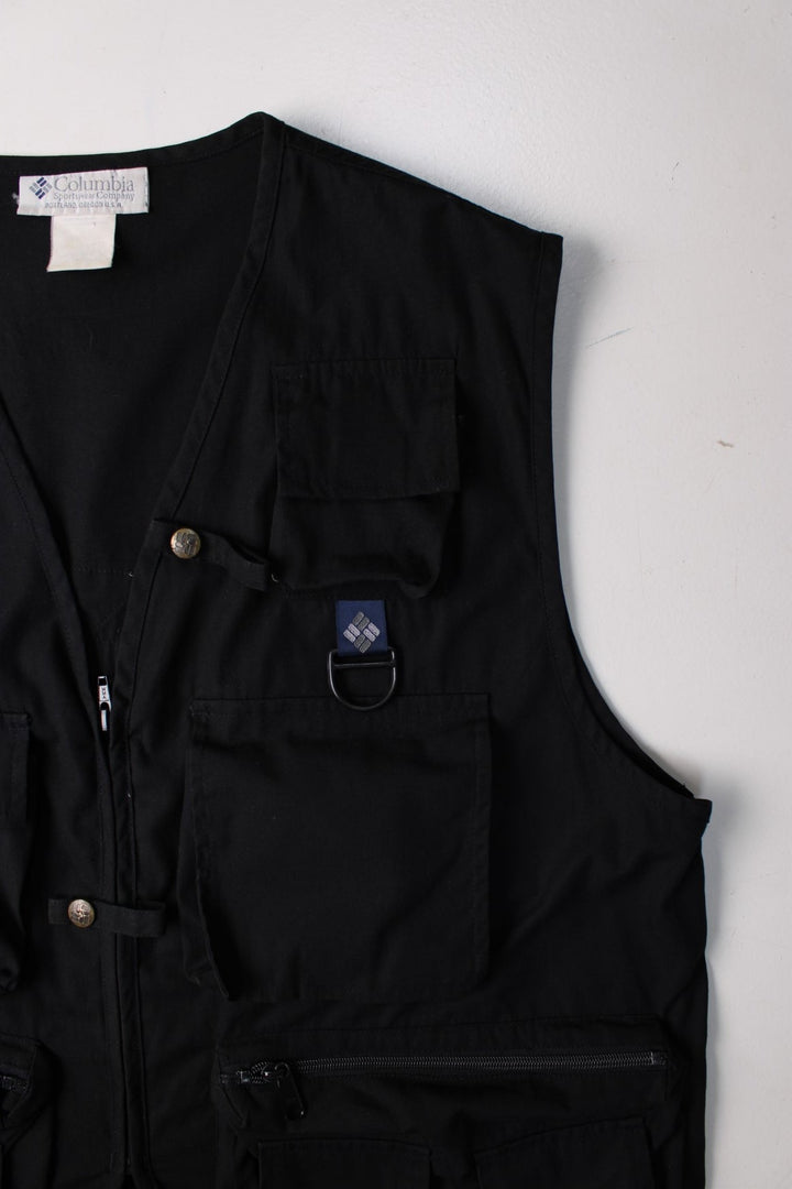 Vintage Columbia PFG Fishing Vest Gilet in a black colourway. Zips up and has multiple utility pockets, and has the logo embroidered on the back.