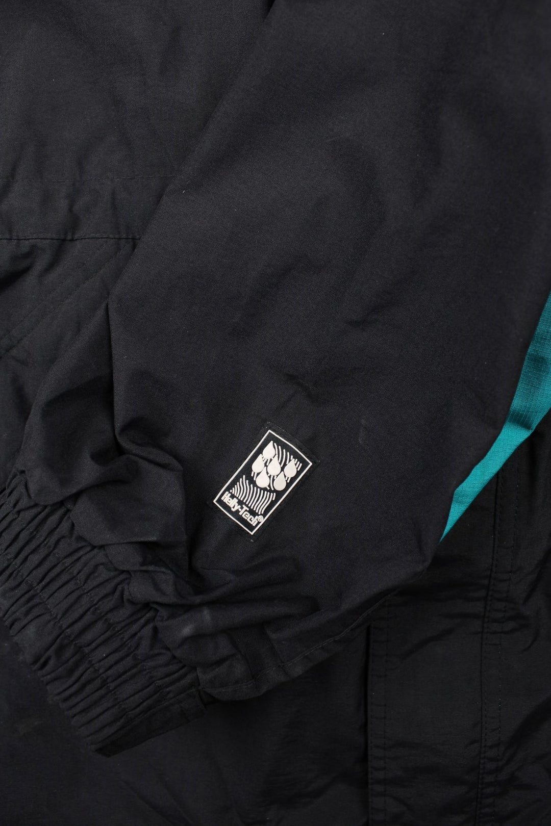 Vintage Helly Hansen Equipe Jacket in a black and blue colourway. Zip and buttons up, has multiple pockets, mesh lining, and has the logos embroidered on the front and left sleeve.