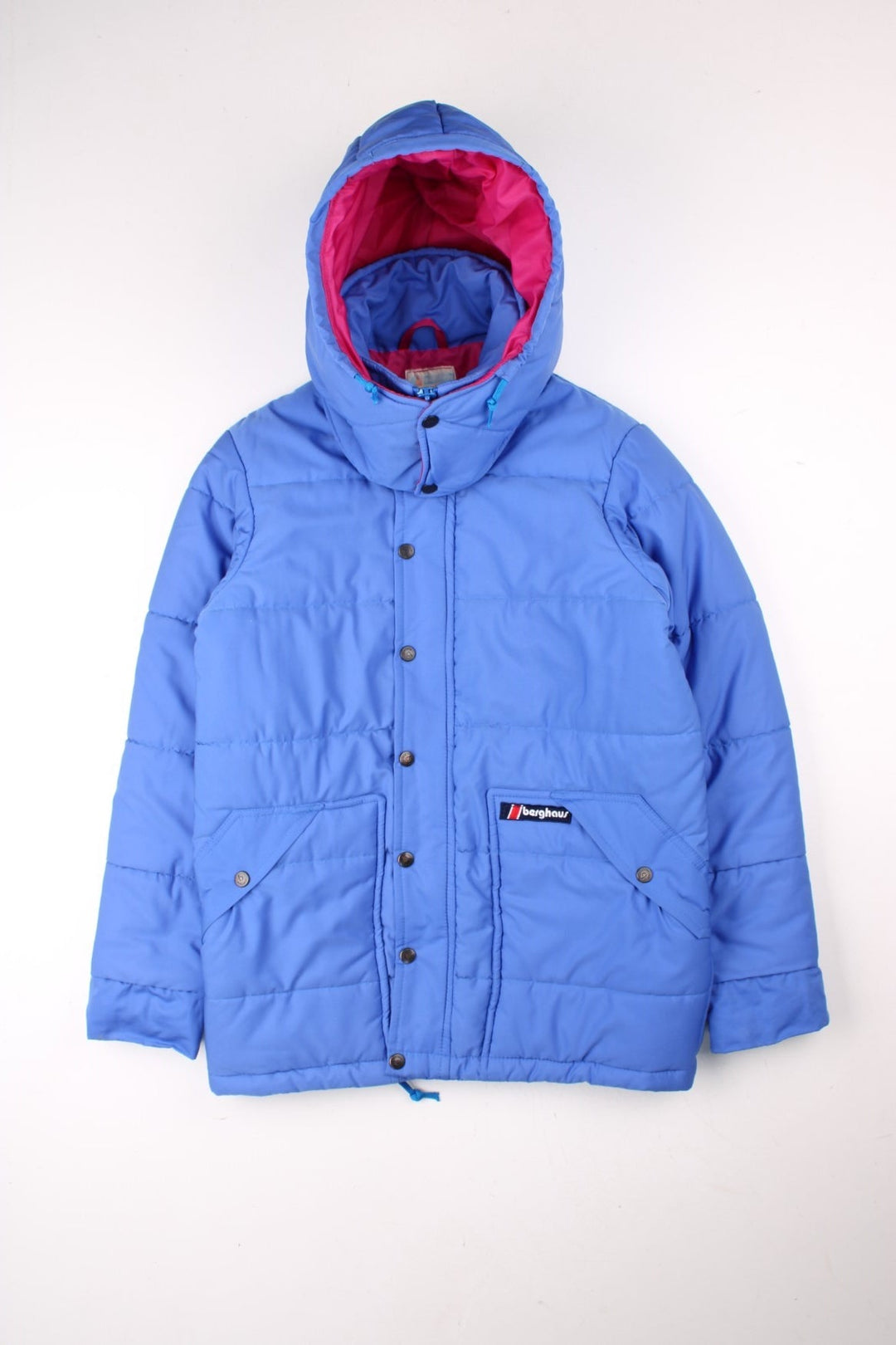 Vintage Berghaus Ice Cap Pole Puffer Jacket in a blue and pink colourway. Zip and buttons up, has side pockets, detachable hood, insulated, and has the logo embroidered on the front.