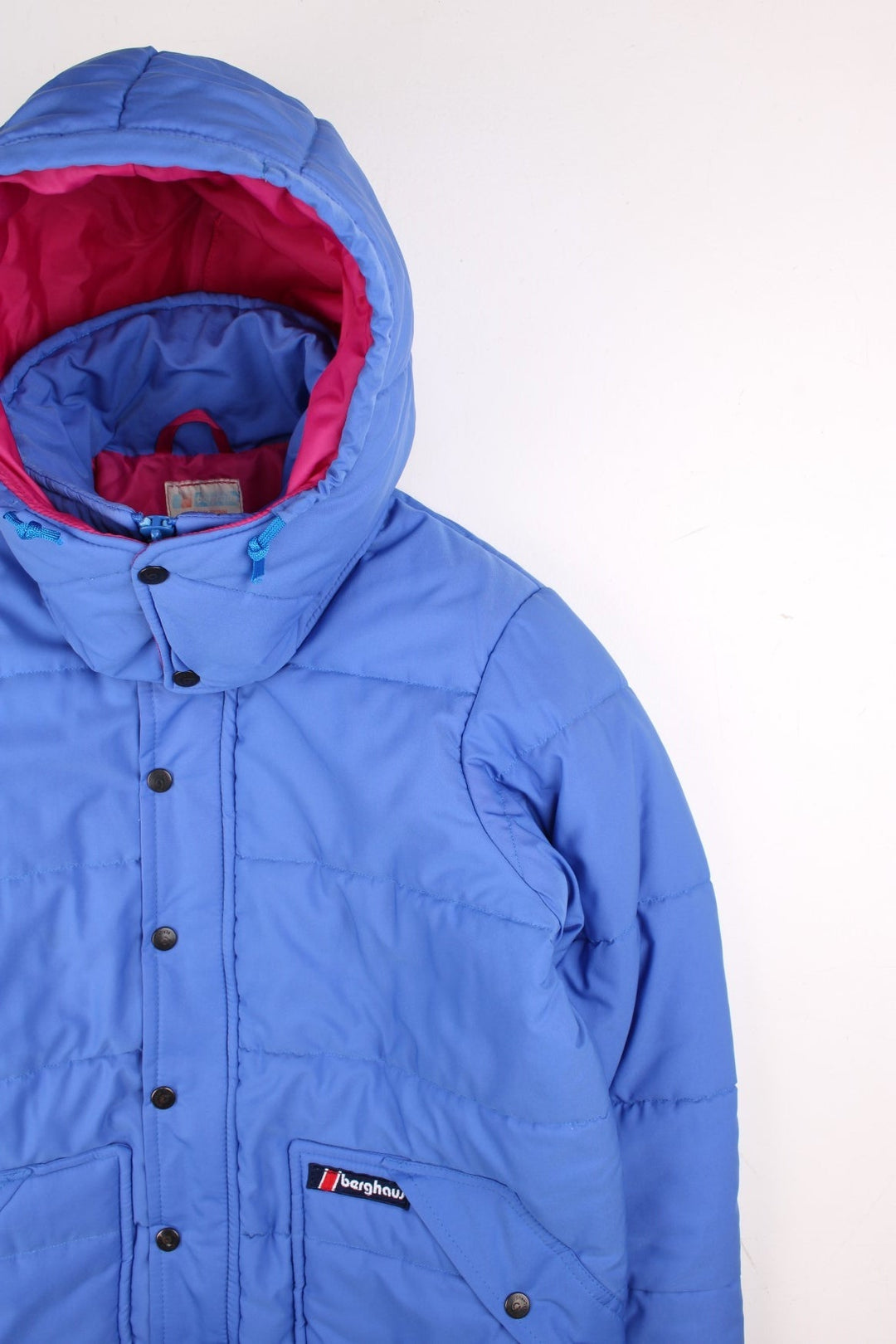 Vintage Berghaus Ice Cap Pole Puffer Jacket in a blue and pink colourway. Zip and buttons up, has side pockets, detachable hood, insulated, and has the logo embroidered on the front.