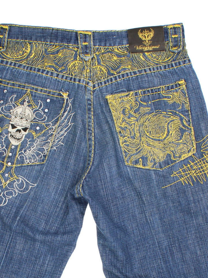 Y2K Victorious Jorts in blue colourway with multiple pockets and has the logo embroidered on the back, as well as contrast patterned cross stitching on the front and back, has skull and bead features.