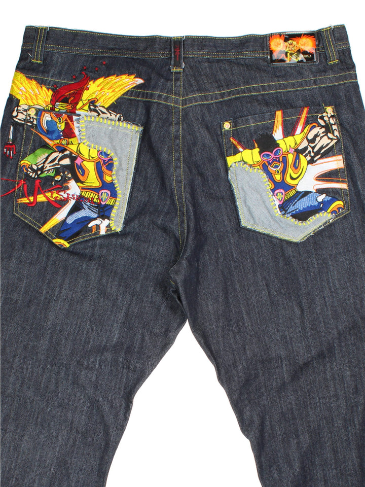 Y2K Miskeen Baggy Jeans in a dark blue colourway with multiple pockets, cross stitching details on the front and on the back has the logo embroidered alongside superhero characters on the pockets.