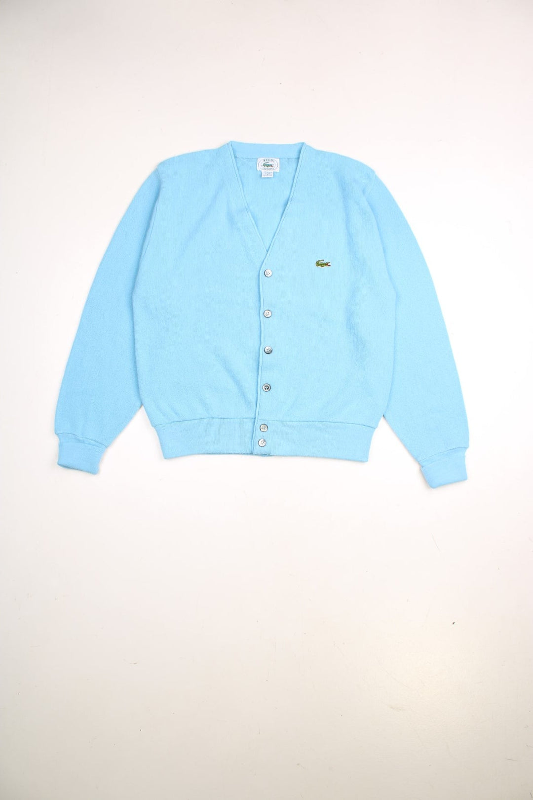 Lacoste jumper in a light blue colourway with the Lacoste logo stitched on the front. The cardigan closes with grey and silver buttons, and has folded cuffs. Made in USA. 