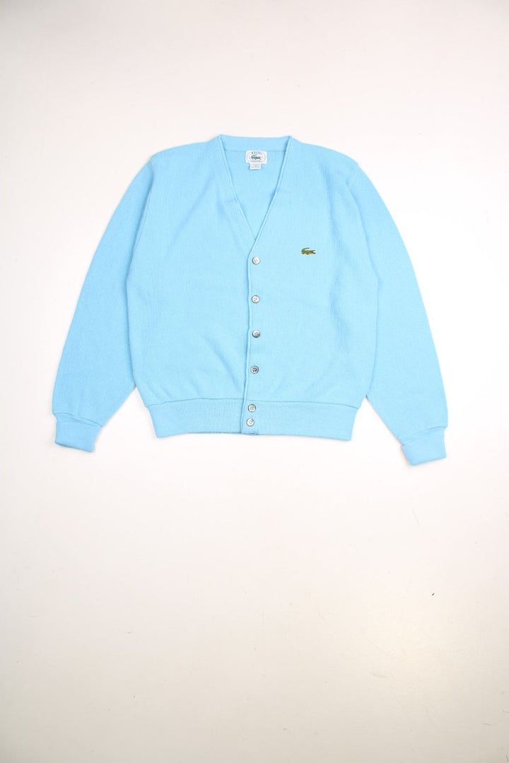 Lacoste jumper in a light blue colourway with the Lacoste logo stitched on the front. The cardigan closes with grey and silver buttons, and has folded cuffs. Made in USA. 