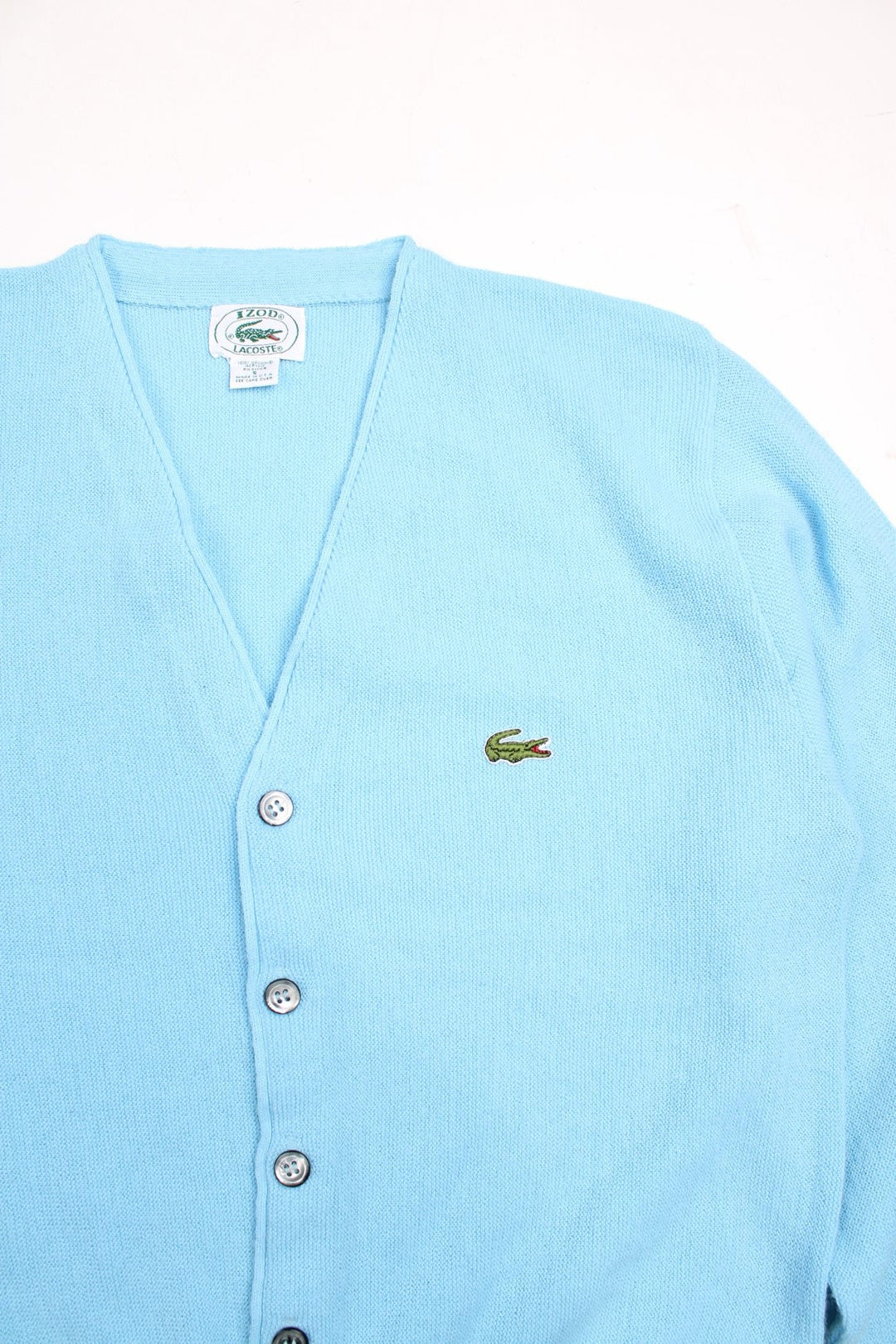 Lacoste jumper in a light blue colourway with the Lacoste logo stitched on the front. The cardigan closes with grey and silver buttons, and has folded cuffs. Made in USA. 