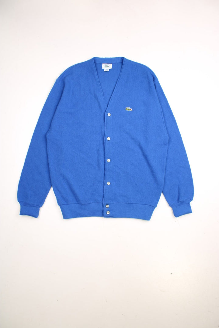 Lacoste jumper in a mid blue colourway with the Lacoste logo stiched on the front. The cardigan closes with grey and silver buttons, and has folded cuffs. Made in USA. 