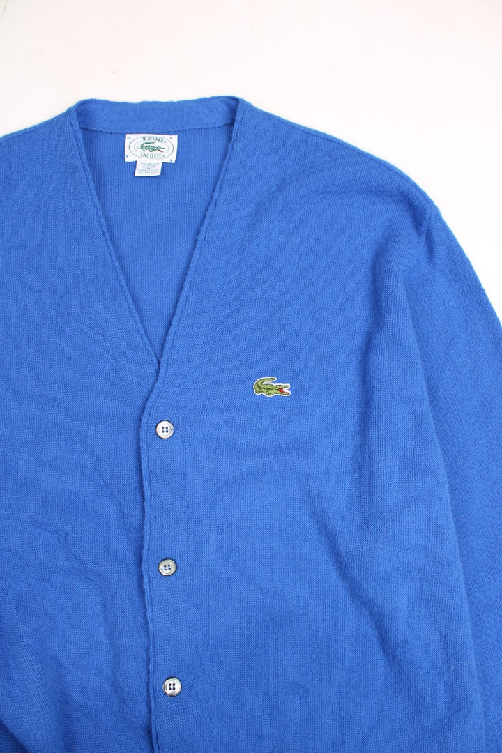 Lacoste jumper in a mid blue colourway with the Lacoste logo stiched on the front. The cardigan closes with grey and silver buttons, and has folded cuffs. Made in USA. 