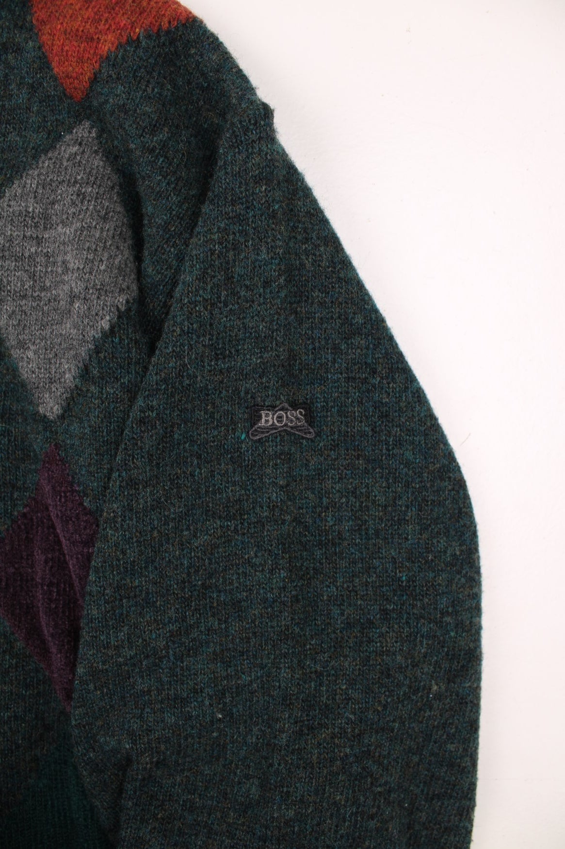 Hugo Boss Knitted Jumper in a green colourway with multicoloured diamond patterns going down the front, has a button up collar and the logo embroidered on the left sleeve. 