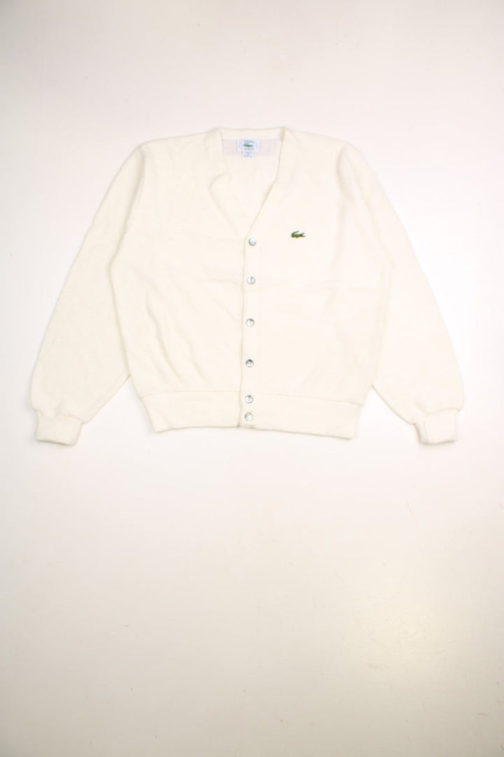 Lacoste cardigan in a off white /creamy colourway with the Lacoste logo stitched on the front. The cardigan has silvery grey buttons and cuffed sleeves. Made in USA. 