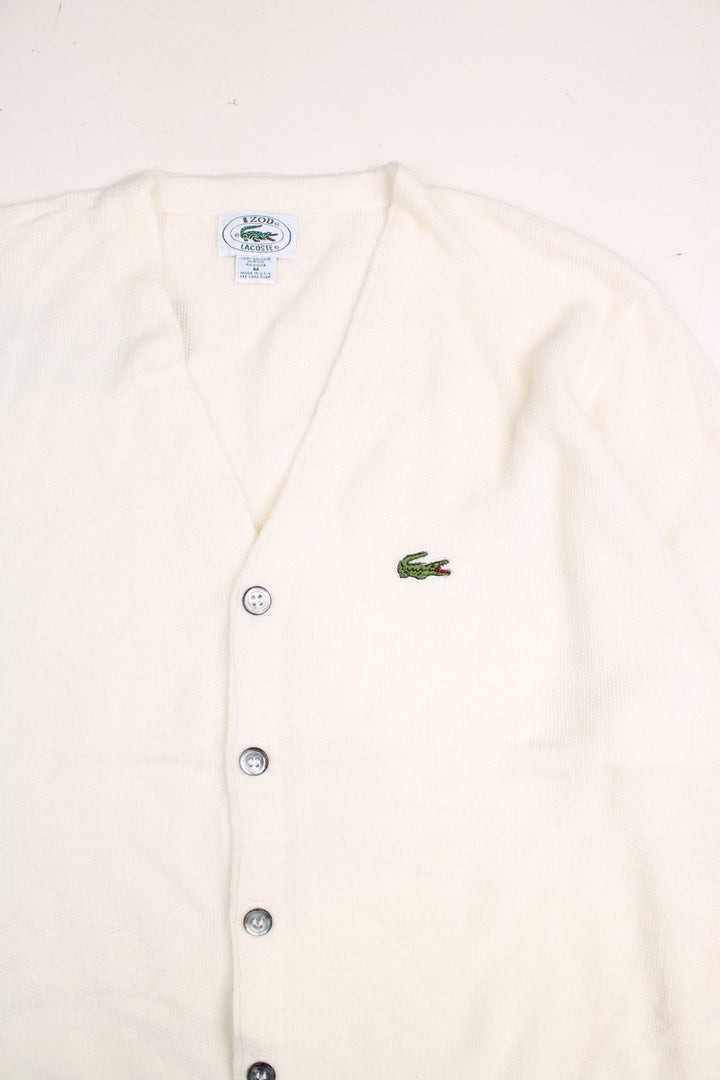 Lacoste cardigan in a off white /creamy colourway with the Lacoste logo stitched on the front. The cardigan has silvery grey buttons and cuffed sleeves. Made in USA. 