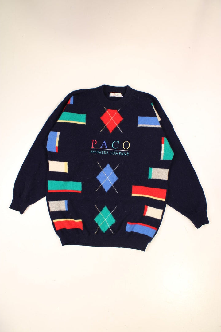 Paco patterned jumper in blue with geometric designs in bright primary colours, and an embroidered spellout reading: 'PACO Sweater Company'.