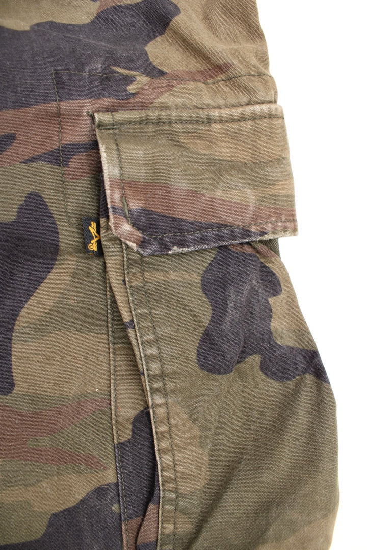 Vintage Alpha Industries Camo Cargo Shorts in a green, black and brown colourway, has an adjustable waist, multiple pockets, and has the logo embroidered on the right pocket.