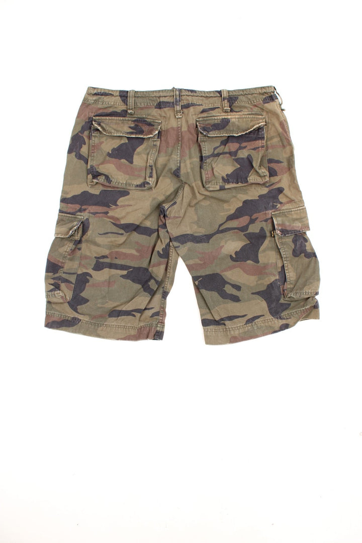 Vintage Alpha Industries Camo Cargo Shorts in a green, black and brown colourway, has an adjustable waist, multiple pockets, and has the logo embroidered on the right pocket.