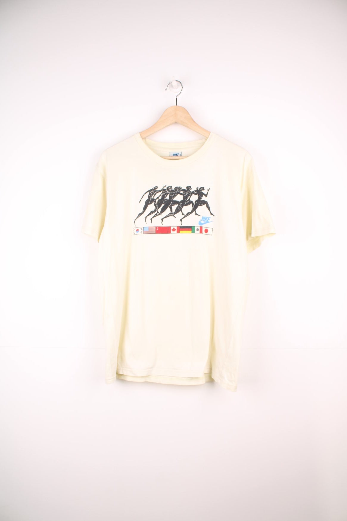 Vintage Nike 1988 Olympic Runners T-Shirt in a pale yellow colourway, has the runners and country flags graphic design printed on the front, as well as the logo and &