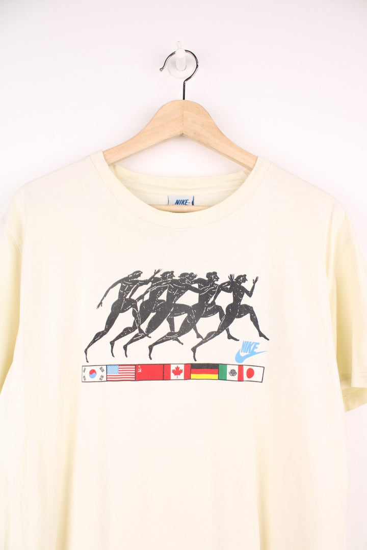 Vintage Nike 1988 Olympic Runners T-Shirt in a pale yellow colourway, has the runners and country flags graphic design printed on the front, as well as the logo and '88' printed on the back. 