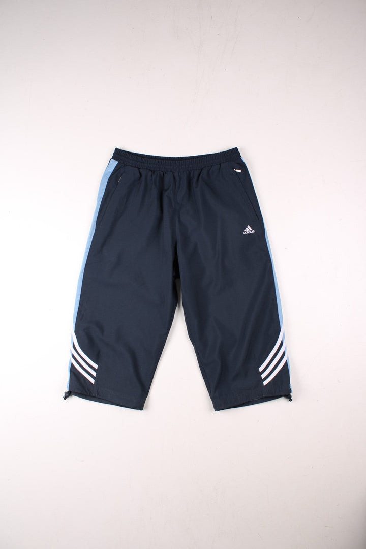 Adidas 3/4 length shorts in navy blue with blue side panels and white three-stripe, an elasticated waist, two zipped pockets and an embroidered logo.