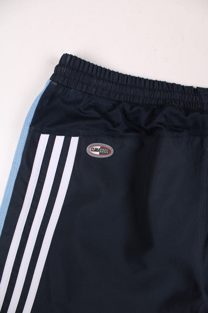 Adidas 3/4 length shorts in navy blue with blue side panels and white three-stripe, an elasticated waist, two zipped pockets and an embroidered logo.