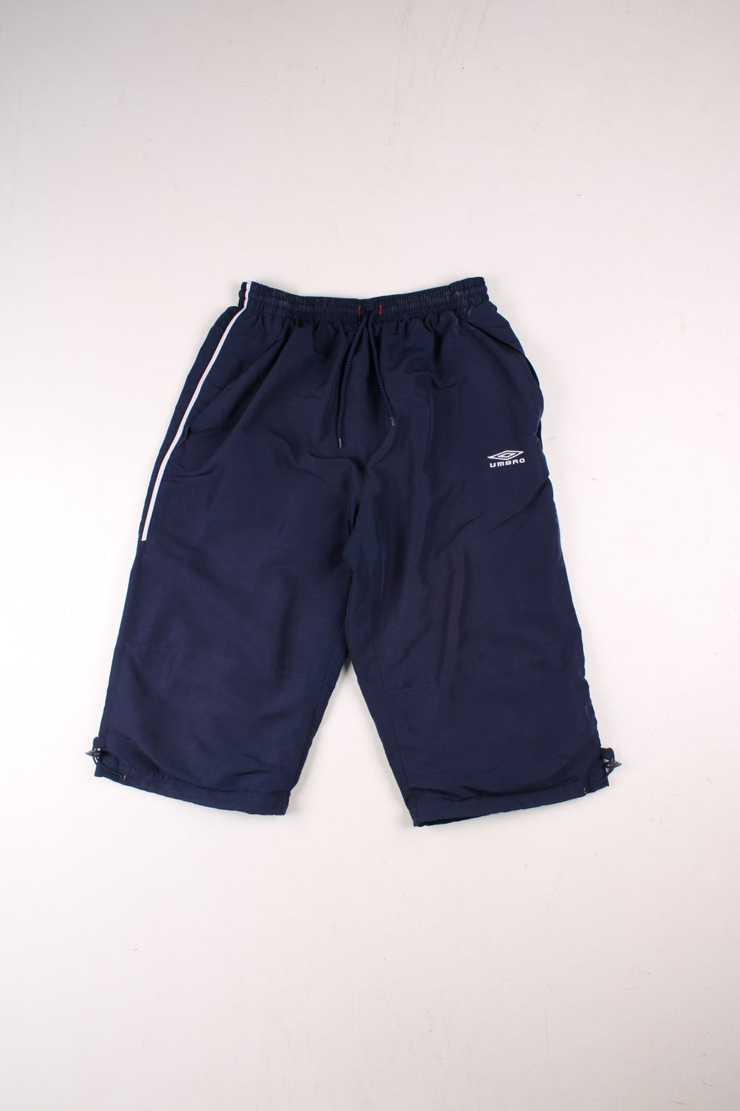 Umbro 3/4 shorts in navy blue with white piping, two pockets, an elasticated waist wirth a drawstring, and an embroidered logo on the front and side.