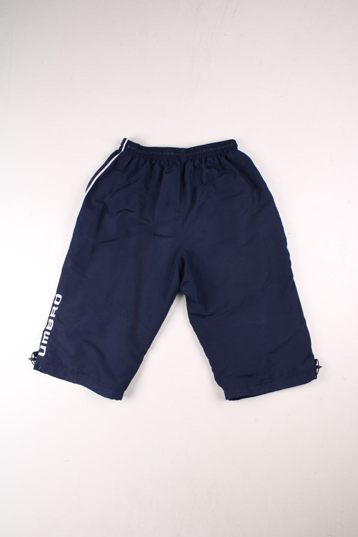 Umbro 3/4 shorts in navy blue with white piping, two pockets, an elasticated waist wirth a drawstring, and an embroidered logo on the front and side.