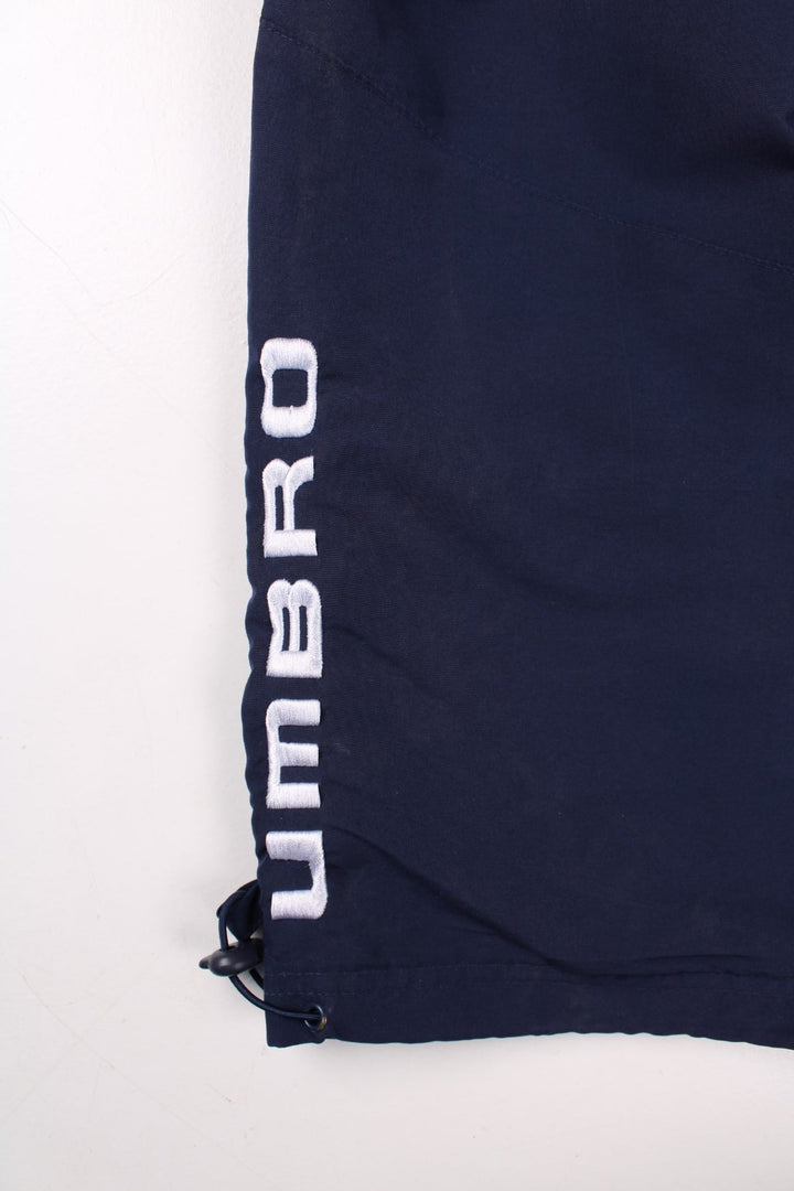 Umbro 3/4 shorts in navy blue with white piping, two pockets, an elasticated waist wirth a drawstring, and an embroidered logo on the front and side.